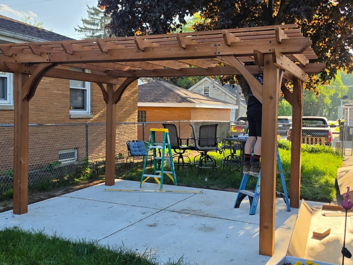 brown pergola installation on concrete patio